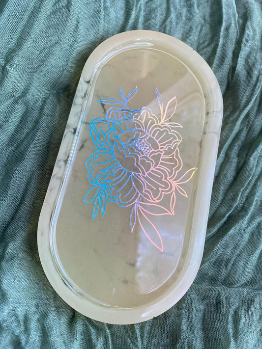 Photo shows an oval-shaped resin tray with a holographic peony illustration in front of a smoky yellow background. The peony is drawn in the style of American traditional tattoos.