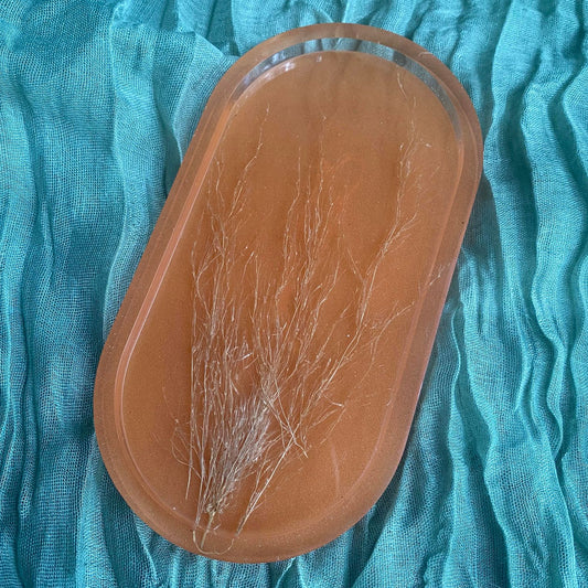 Photo shows an oval-shaped resin tray with a terra cotta background, with tan pampass grass in the foreground.