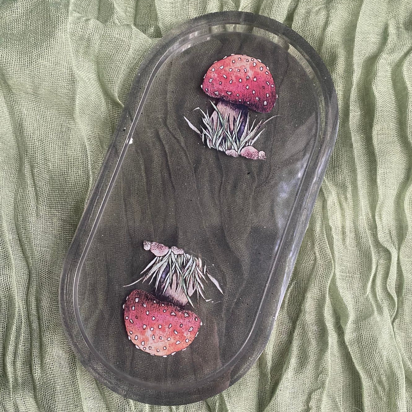 Photo shows an oval-shaped resin tray with illustrated mushroom stickers inside in front of a transparent black background.