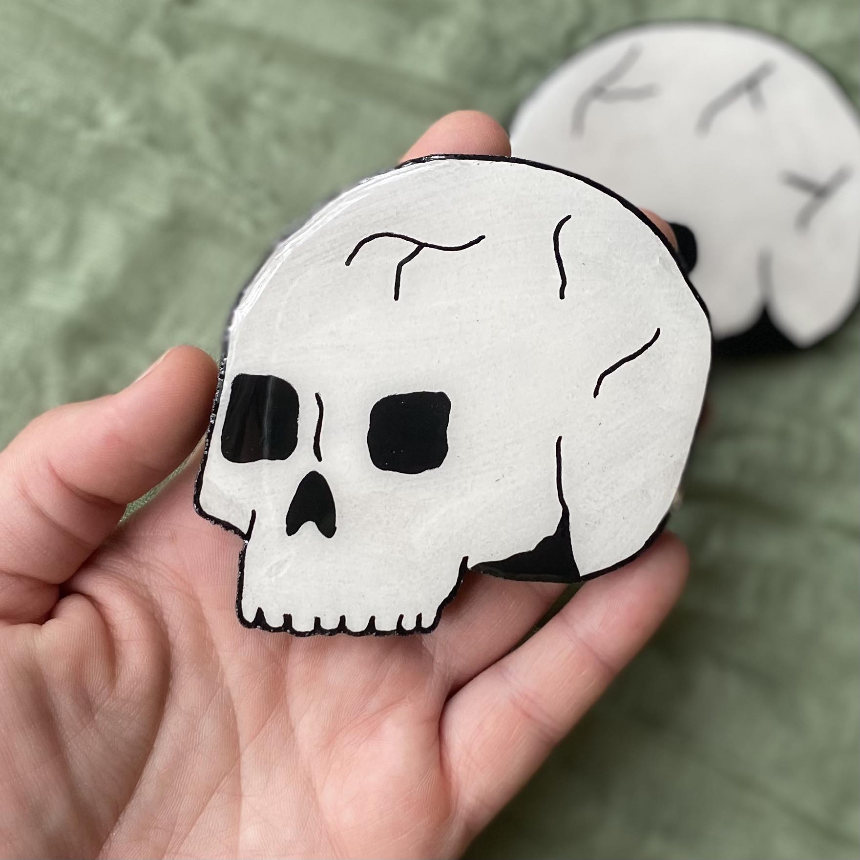 This magnet is a white skull, with no jaw. There are cracks painted at the top of the skull and black outlines for all the other details.