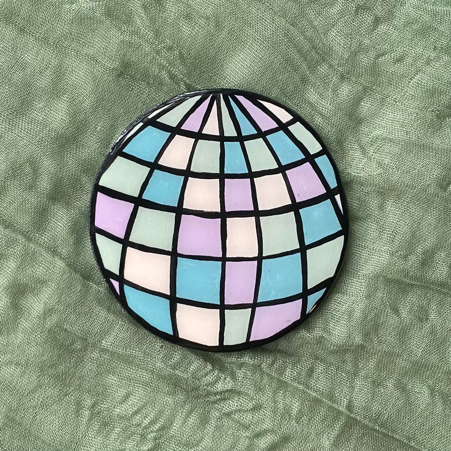 This disco ball magnet is round with black outlines separating each section of mirror. Each mirror section is painted in a different pastel color.