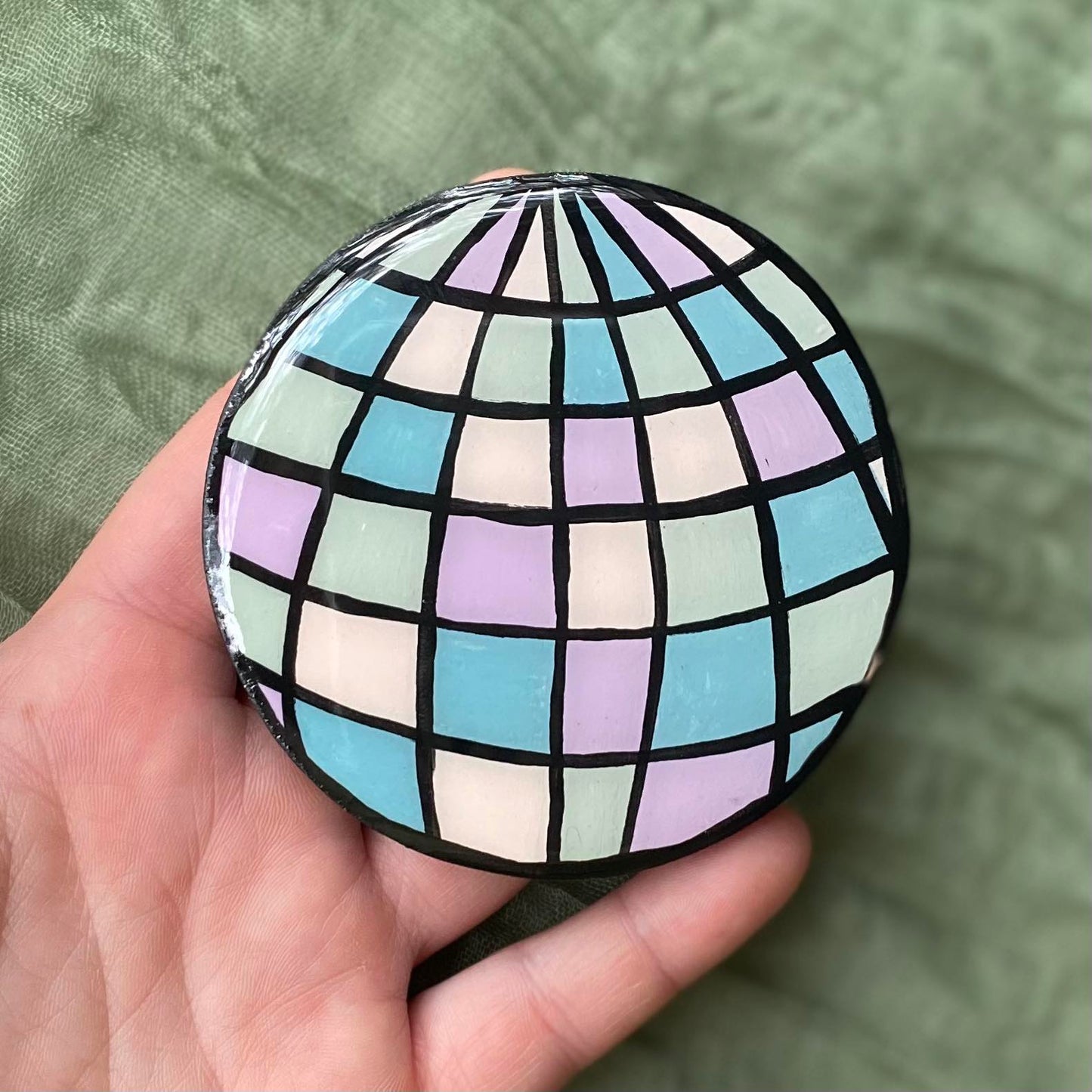 This disco ball magnet is round with black outlines separating each section of mirror. Each mirror section is painted in a different pastel color.