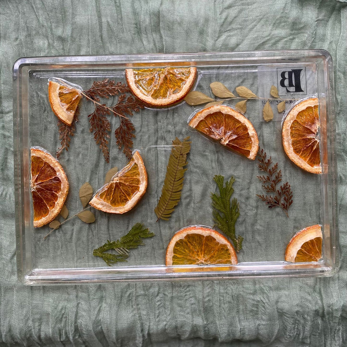 Photo shows a clear, rectangle-shaped resin tray with segments of real oranges and dried ferns in the background.